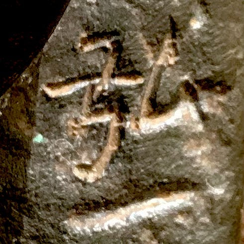 Primer plano de la marca de Hirokazu Mizushima en la escultura de bronce de dos ciervos. La luz resalta los caracteres incisos sobre el metal oscuro y texturizado, con restos de pátina verde alrededor de los trazos.