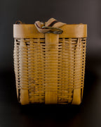 Narrow end of a vintage Japanese bamboo biku fishing basket, with the striped fabric strap folded over its broad rim. Fine horizontal bamboo strips cross wider upright ribs, with darker patches near the base.
