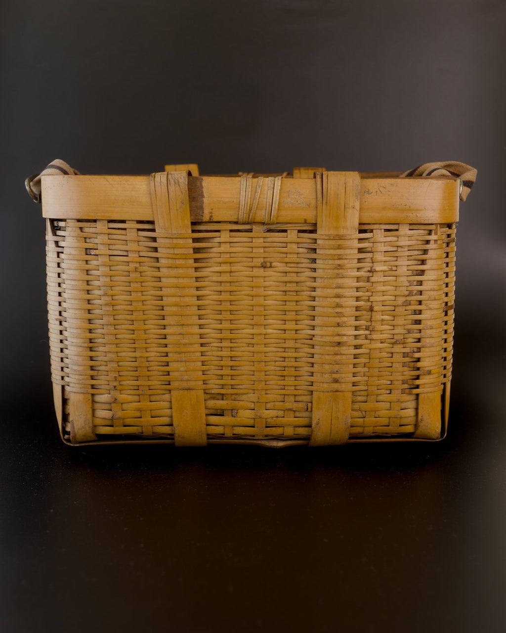 Broad side of a vintage Japanese biku fishing basket. Golden bamboo strips form a close horizontal weave beneath a thick rim, reinforced by two wide vertical bands. Thin bamboo bindings wrap around the center of the rim.