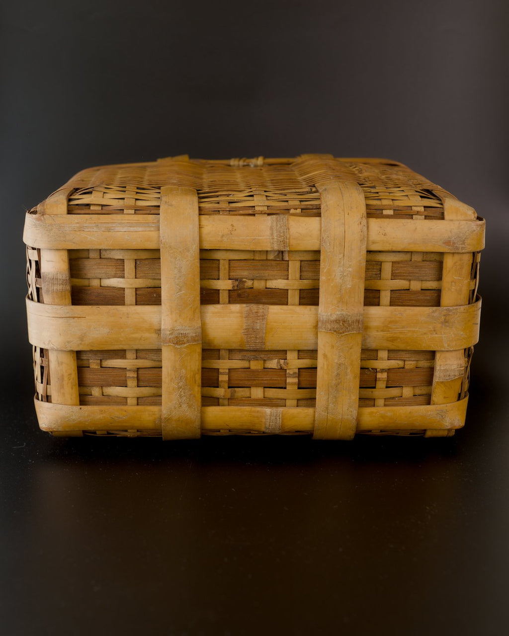 Underside of a vintage Japanese biku fishing basket, resting upside down. Wide golden bamboo strips form a rectangular grid reinforced by broad crossing bands, with pale scuffs and darker areas on the bamboo.
