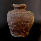 Antique Shigaraki stoneware jar photographed against a dark background, showing its reddish brown, pitted clay body, flared rim, and incised cypress-fence pattern around the shoulder.