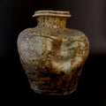 Antique Shigaraki stoneware jar with a flared rim, incised shoulder decoration, pale green ash glaze, and a deeply slumped section of its rounded body.