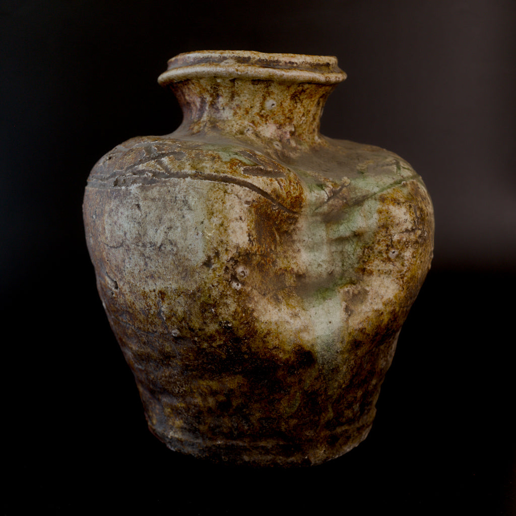 Antique Shigaraki stoneware jar with a wide rolled rim, mottled brown and cream surface, incised shoulder design, and greenish ash glaze flowing over the collapsed side.
