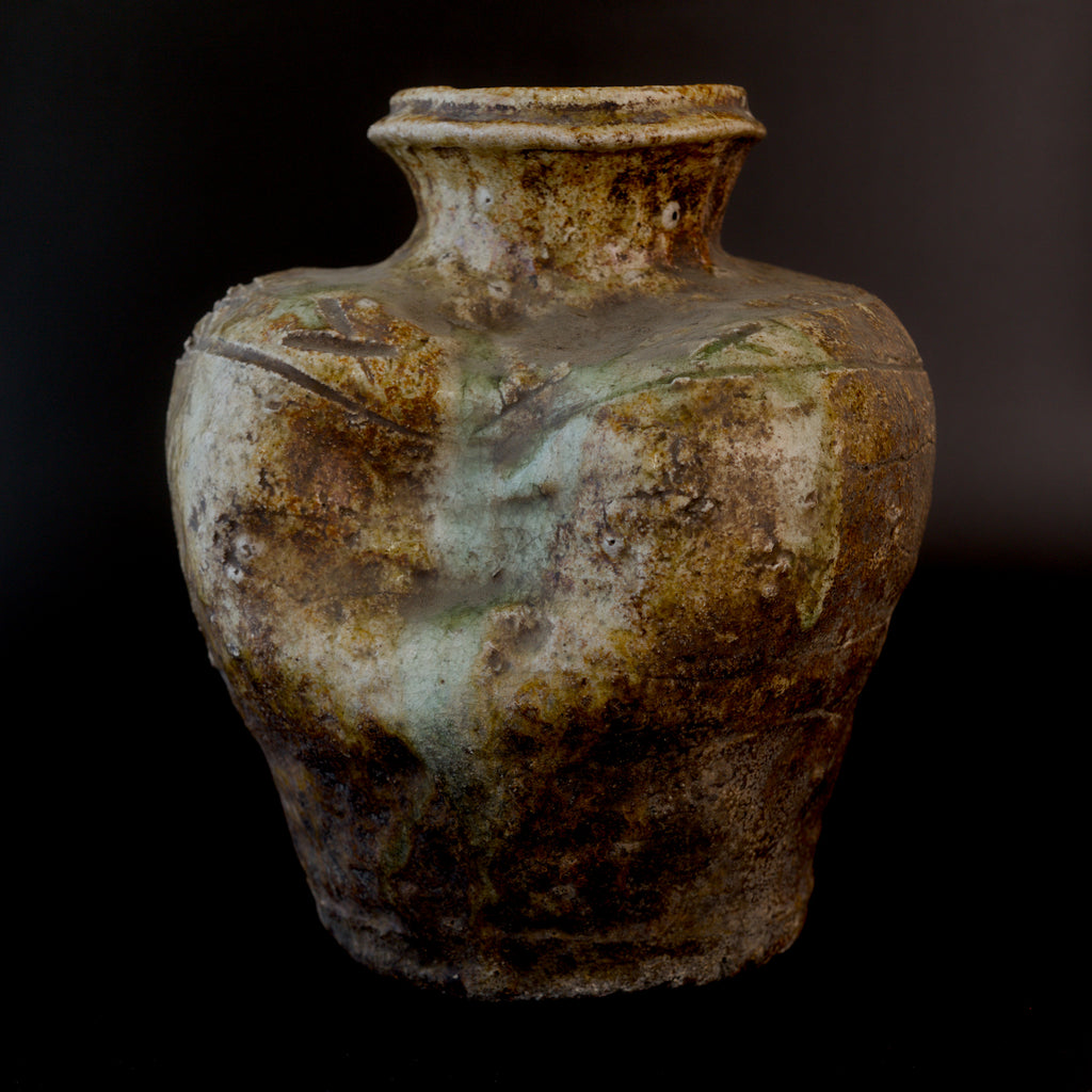 Front view of an antique Shigaraki stoneware jar with a rolled lip, incised geometric shoulder decoration, a sunken upper shoulder, and pale green ash glaze running down the body.