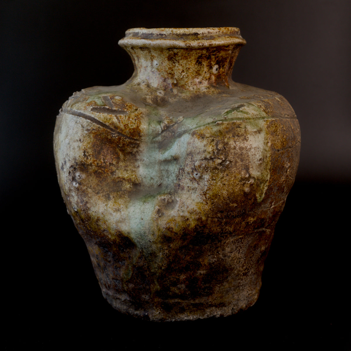 Front view of an antique Shigaraki stoneware jar with a rolled lip, incised geometric shoulder decoration, a sunken upper shoulder, and pale green ash glaze running down the body.