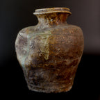Three-quarter view of an antique Shigaraki jar with a flared neck, reddish brown stoneware, incised lines around the shoulder, and pale green ash glaze running down one side.