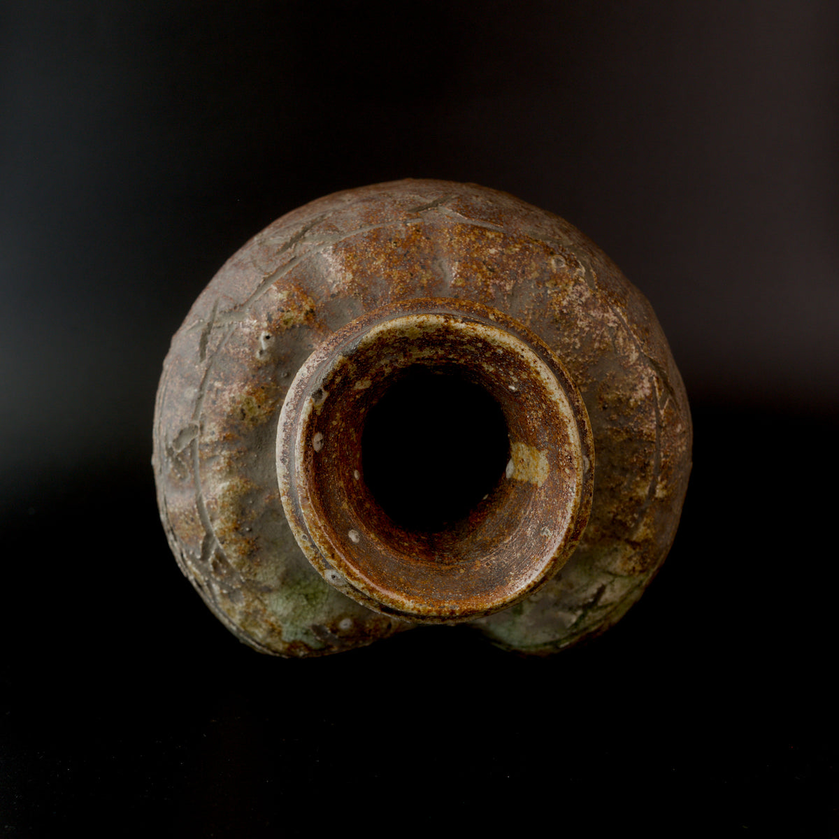 Overhead view into an antique Shigaraki stoneware jar, showing its thick round rim, dark mouth, uneven shoulders, incised lines, and mottled brown and green ash-glazed surface.